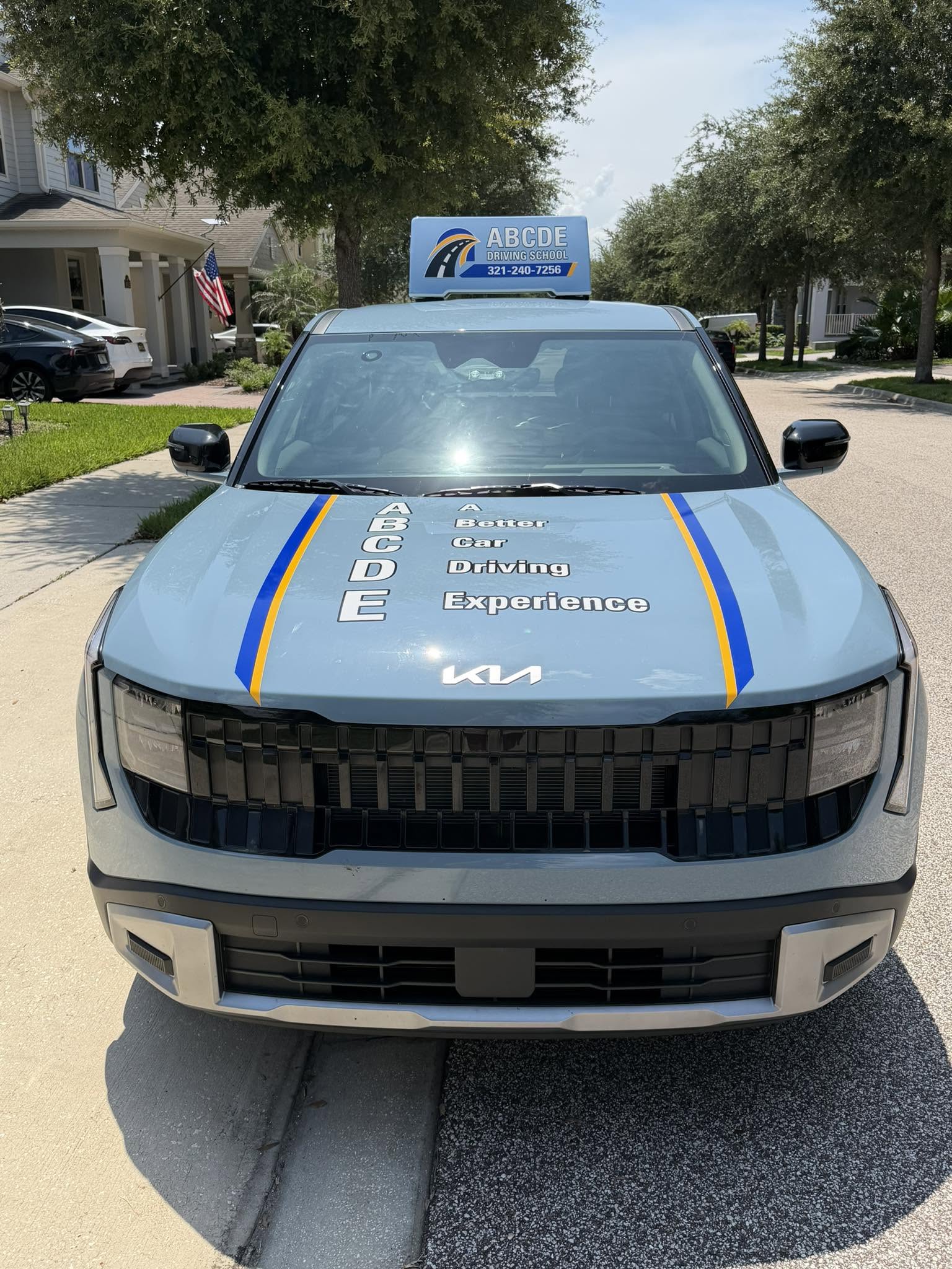 Front view of ABCDE Driving School’s blue Kia Seltos with branded hood and roof sign